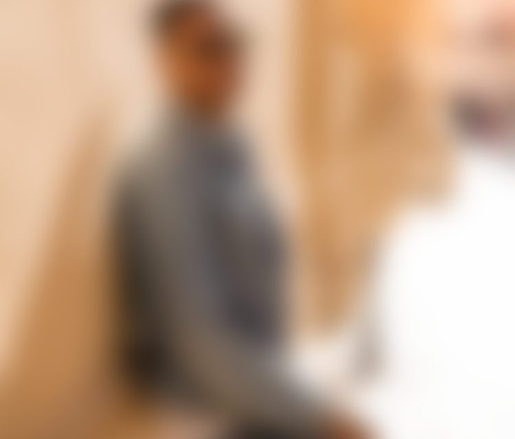 Blurred person sitting indoors by beige wall